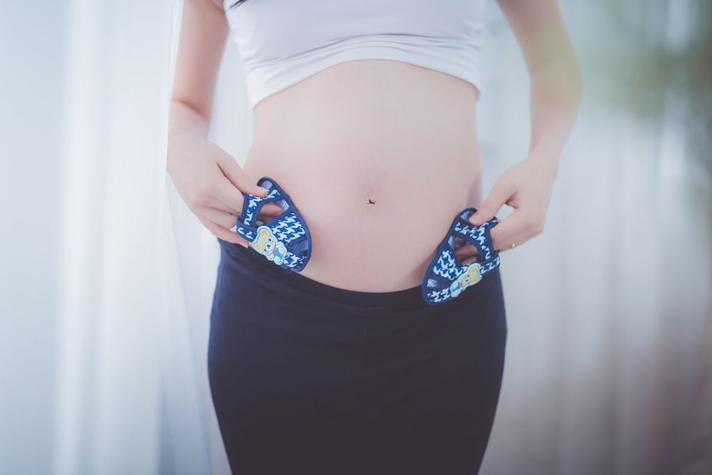 A pregnant woman holds baby shoes near her belly, symbolizing anticipation and joy.