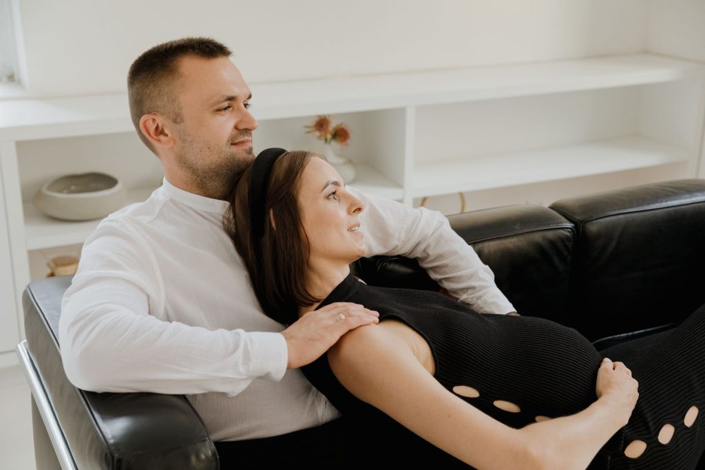 A loving expectant couple sits on a sofa, enjoying a peaceful moment together.