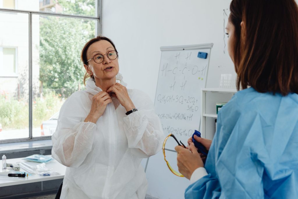 Two healthcare professionals in PPE discussing information in a bright lab.