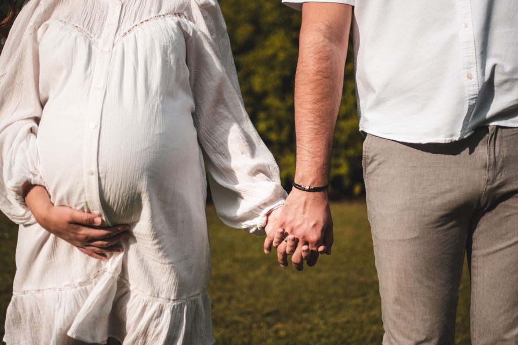 A pregnant woman and man holding hands outdoors, symbolizing love and family.